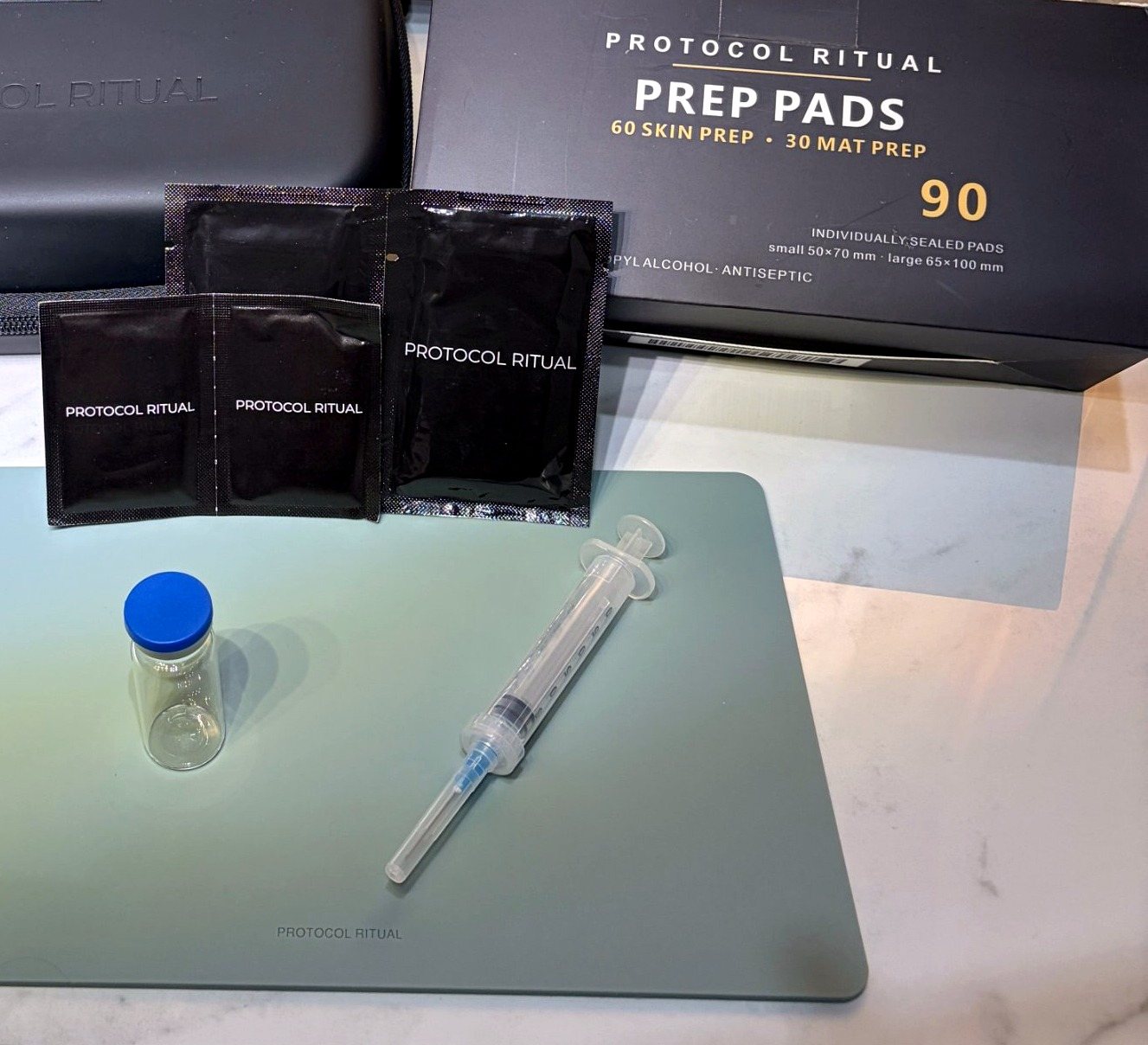 Protocol Ritual prep pads, the box of 90 and a slate reconstitution mat with a vial and syringe